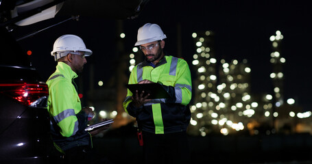 Industrial System Engineers Discussing Over Laptop And Digital Tablet While work over night at Refinery and gas petrochemical plant
