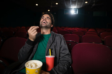 Moviegoer sitting alone in cinema holding yellow popcorn bucket and red drink under projector beam