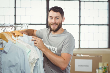 Male volunteer sorting donated shirts on wooden hangers beside donation boxes at warehouse