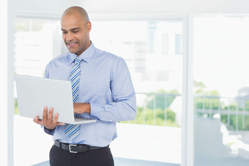 Fototapeta premium Man in his 30s wearing striped tie standing while holding laptop at modern office with skyline