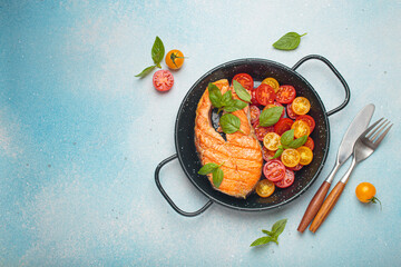 Grilled salmon steak on a black pan, accompanied by vibrant cherry tomatoes and fresh basil leaves, healthy eating or diet concept, copy space