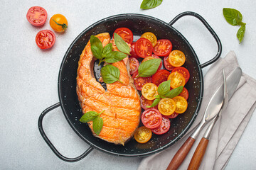 Grilled salmon steak on a black pan, accompanied by vibrant cherry tomatoes and fresh basil leaves, healthy eating or diet concept