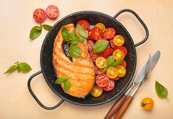 Grilled salmon steak on a black pan, accompanied by vibrant cherry tomatoes and fresh basil leaves, healthy eating or diet concept