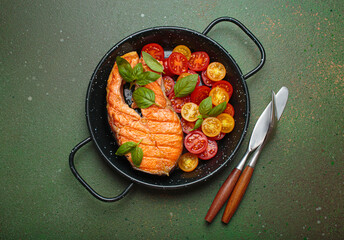 Grilled salmon steak on a black pan, accompanied by vibrant cherry tomatoes and fresh basil leaves, healthy eating or diet concept
