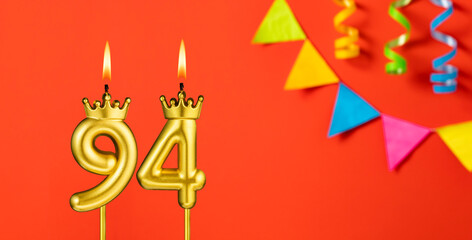 Number 94 birthday candle on an orange background with pennants