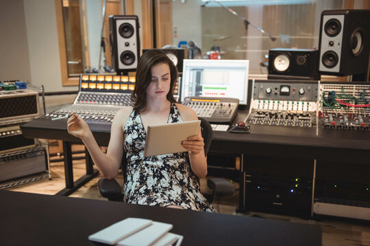 Adult woman holding tablet while reviewing audio tracks on mixing desk in recording studio
