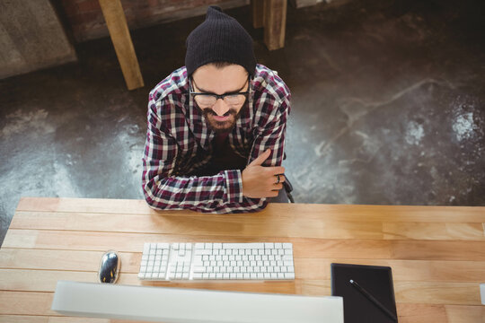 Man leaning on wooden desk in studio with keyboard and mouse using graphics tablet with stylus