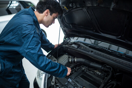 Open car hood revealing engine components inside automotive repair workshop with vehicles parked