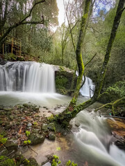 Obraz premium Wooden walkways over a waterfall in a lush forest, surrounded by moss-covered rocks and tall trees, creating a serene scene, located in Pindelo, Outeiro, Oliveira de Azemeis, Portugal
