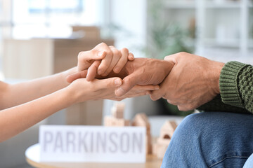 Senior man suffering from Parkinson syndrome with woman holding hands at home, closeup