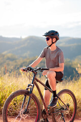 Fototapeta premium Young man resting on his mountain bike after a trail ride in nature. Promoting an active lifestyle, outdoor fitness, and personal well-being.
