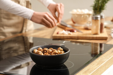 Woman and frying pan with roasted mushrooms on electric stove in kitchen