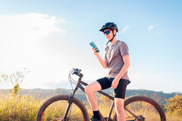 Obraz premium Young cyclist using a smartphone during a break on a mountain biking trail. Concept of outdoor connectivity, fitness tracking, and modern lifestyle.