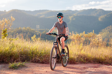 Man cycling on a dirt trail surrounded by nature, during golden hour. Concept of healthy lifestyle,...