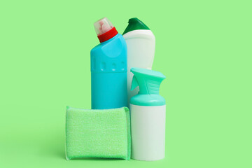 Bottles of detergents with cleaning sponge on green background