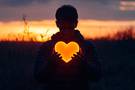 Man holding a glowing heart in his hands silhouette - Powered by Adobe