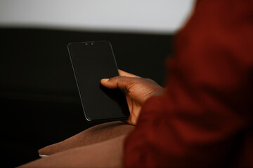 Black African male person Hand sitting holding mobile phone with black blank screen in living room, social media, news, entertainment