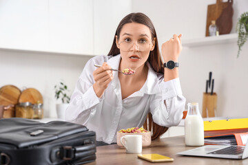 Hurrying young businesswoman with wristwatch eating cereal rings in kitchen