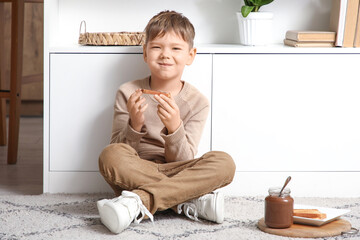 Cute little boy eating toast with sweet chocolate paste in kitchen