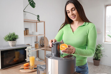 Young woman making orange juice at table in kitchen