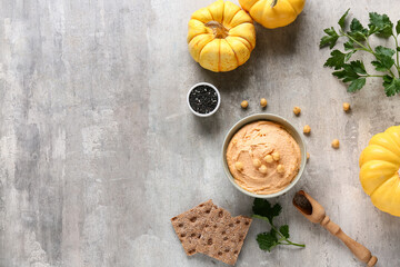 Bowl of tasty hummus with pumpkins, parsley and crackers on grey grunge background
