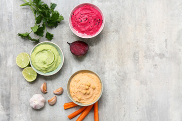 Bowls of different tasty hummus with parsley, beet and carrot on grey grunge background
