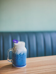 Butterfly pea milk tea. A glass of blue drink milk tea topping with milk foam and a petal of butterfly pea on the wooden table, copy space background for your text. Soft focus.