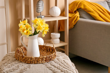 Wicker tray with vase of beautiful yellow daffodils bouquet on ottoman in room