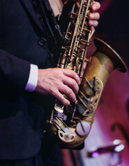 Obraz premium Concert view of saxophonist musician, saxophone sax player with vocalist and musical band during jazz orchestra show performing music on a stage in the scene lights, concert in a musical club hall