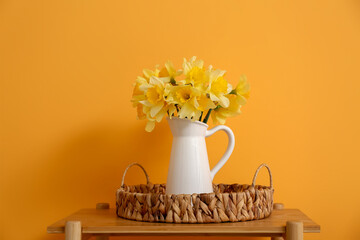 Wicker tray with vase of beautiful daffodils bouquet on shelving unit near yellow wall in room