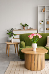 Interior of light living room with green sofa, table and tulips in vase