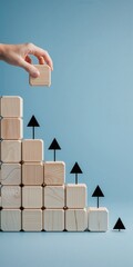Hand placing final wooden block with upward arrow on staircase pattern against light blue background