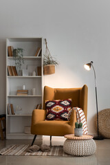 Interior of living room with armchair, bookshelf and glowing lamp in evening