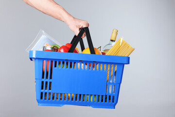 Fototapeta premium Man holding shopping basket with different products on grey background, closeup