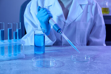 Scientist taking sample with micropipette out of Petri dish at table in laboratory, closeup