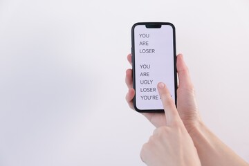 Cyber bullying. Woman holding smartphone with insults on light background, closeup. Space for text
