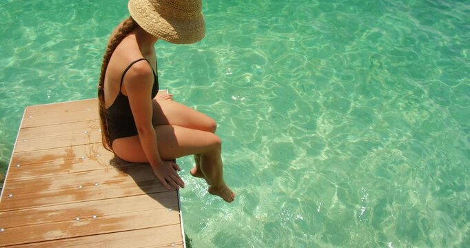 Woman sitting on dock with feet in clear sea water on sunny day in summer Croatia