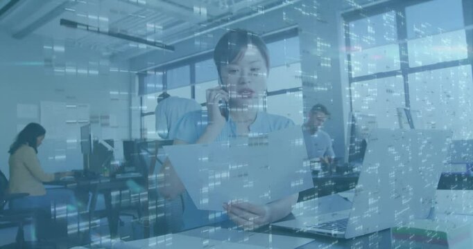 businesswoman at desk answering call while reviewing documents and checking time with data stream