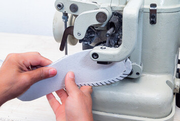 Woman's hands operating an industrial sewing machine to sew the leather sole for handmade shoes in the shoemaking workshop, close-up of the traditional shoemaking process. 