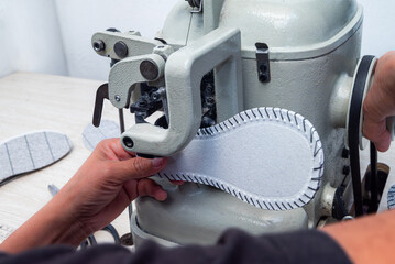 Woman's hands operating an industrial sewing machine to sew the leather sole for handmade shoes in the shoemaking workshop, close-up of the traditional shoemaking process. 