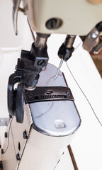 Close-up of a post-bed sewing machine used in the shoemaking industry, stitching leather with...