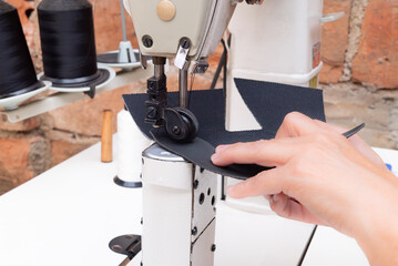 A woman's hands sewing fabric with an industrial sewing machine in a shoemaking workshop. Close-up of the manual labor and textile manufacturing process.