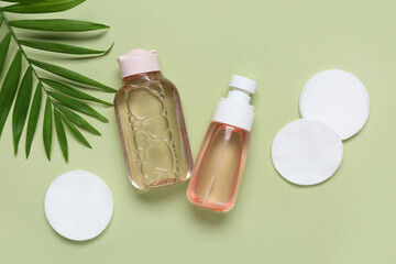Bottles of micellar water, cotton pads and leaves on green background