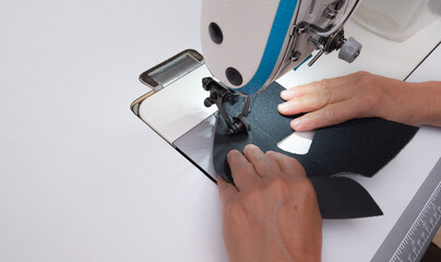 A woman's hands sewing fabric with an industrial sewing machine in a shoemaking workshop. Close-up of the manual labor and textile manufacturing process.