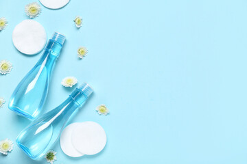 Bottles of micellar water, cotton pads and flowers on blue background