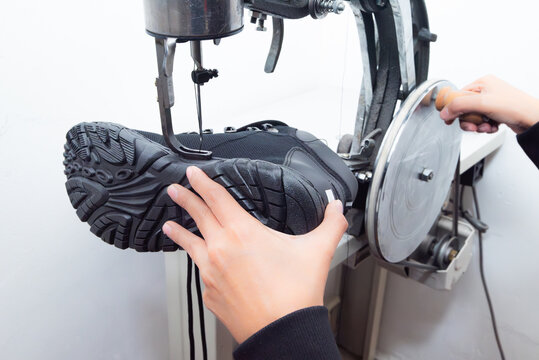 Shoe repair with industrial sewing machine and hands stitching a black trekking boot sole.
