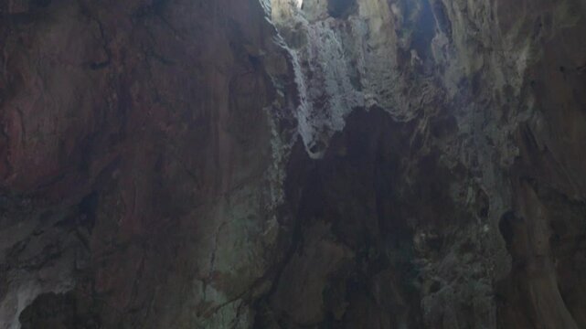 Rocky cavern interior with sunlight piercing ceiling, highlighting lone traveler standing beneath natural light beam, silently observing dramatic geological surroundings