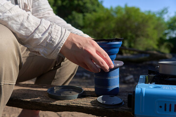 Process of making coffee outdoors, an unrecognizable traveler places the folding travel filter over...