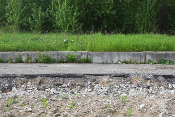 A broken and abandoned paved sidewalk near a green lawn