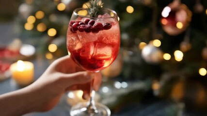 Two festive cranberry cocktails with ice and rosemary garnish, held in front of holiday lights, creating a celebratory atmosphere. - Powered by Adobe